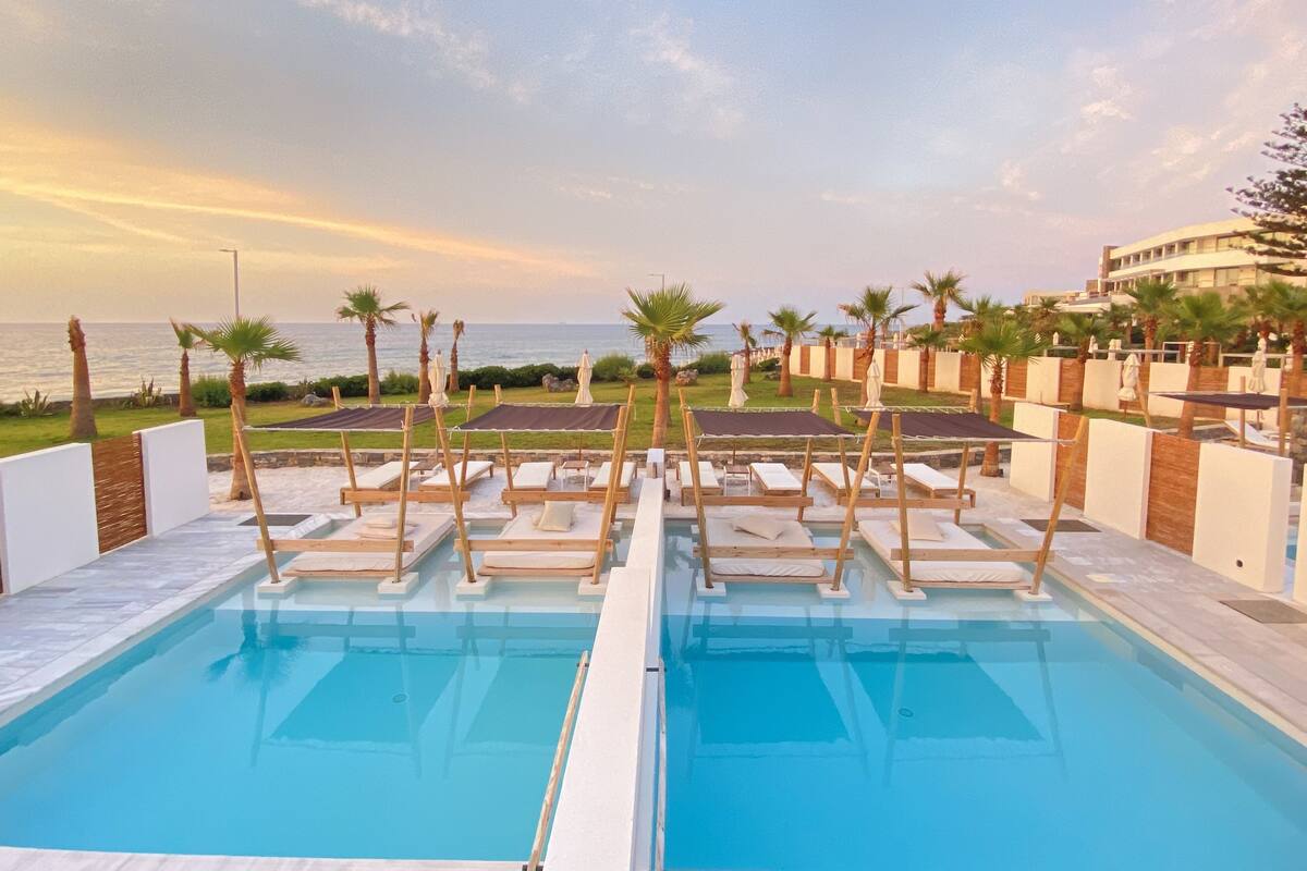 Zona de piscina con tumbonas y sombrillas, con vistas a una playa y al océano.