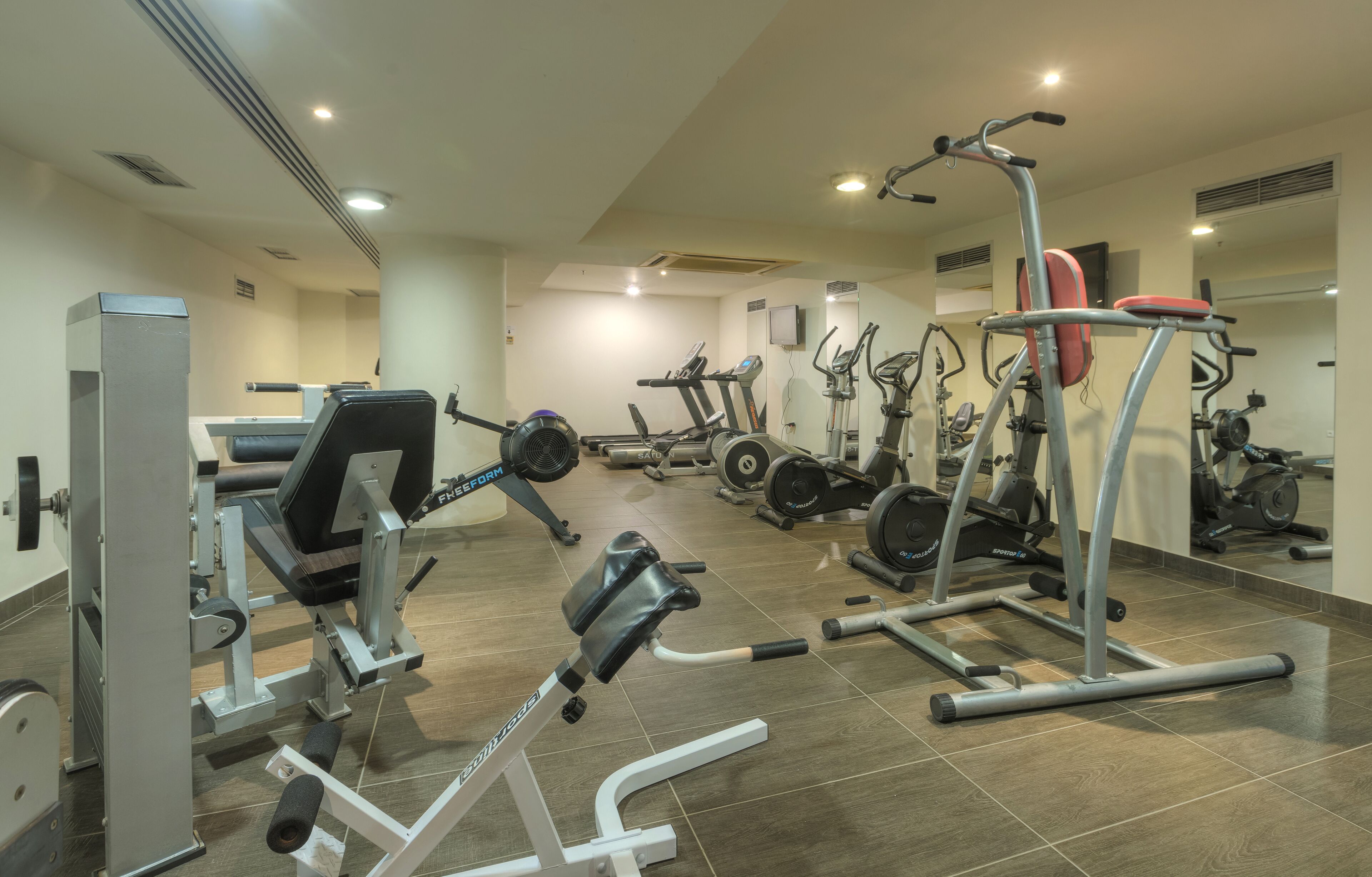 A gym with various exercise machines, including treadmills and weight stations, arranged in a spacious layout.