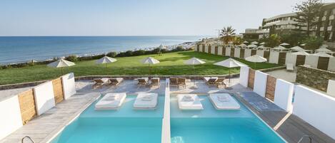 A pool area with two pools, lounge chairs, umbrellas, and a view of the ocean.