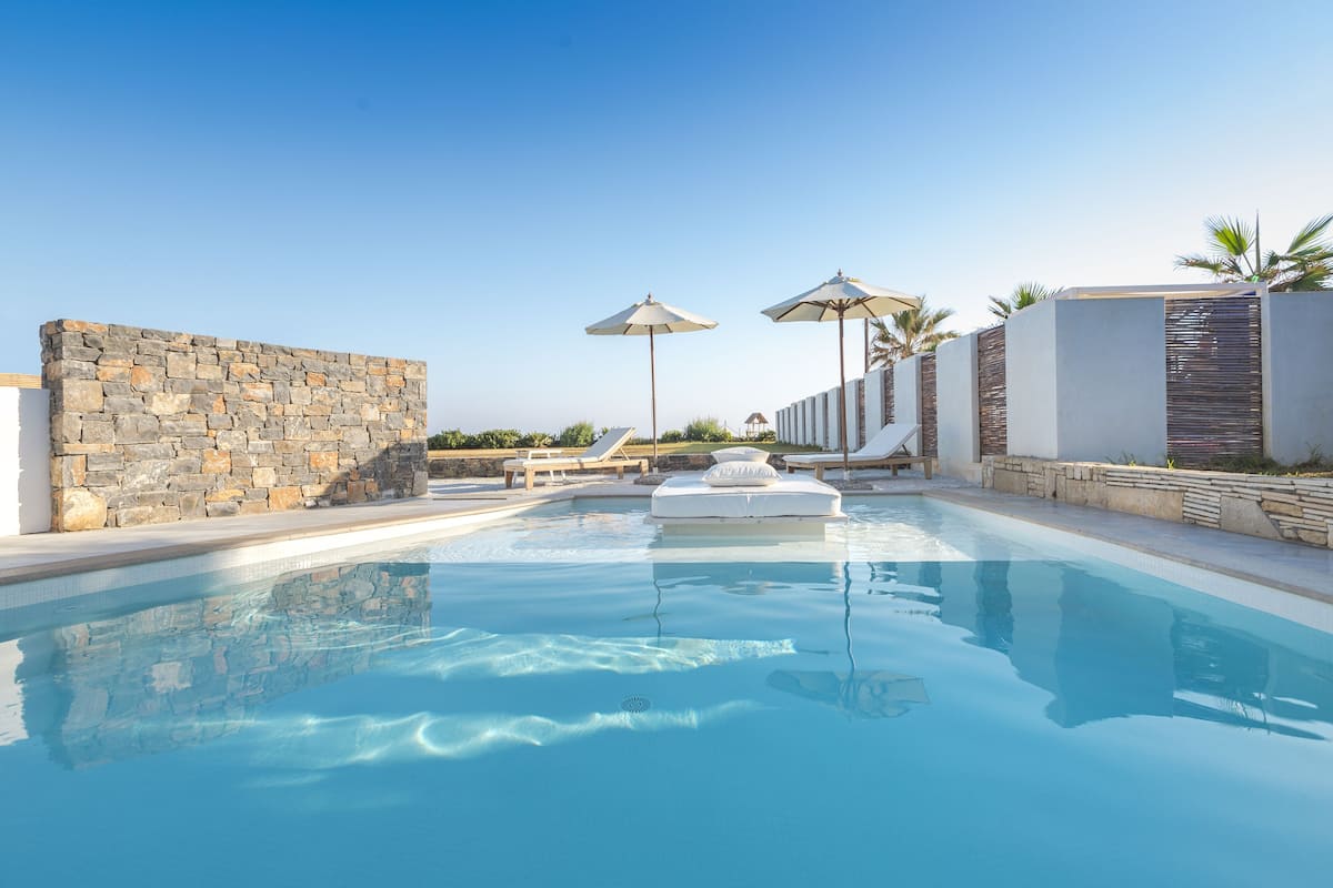 Una piscina con paredes de piedra, sillones de descanso y sombrillas.