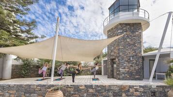 Un espacio al aire libre moderno para yoga, con un muro de piedra y un toldo grande.