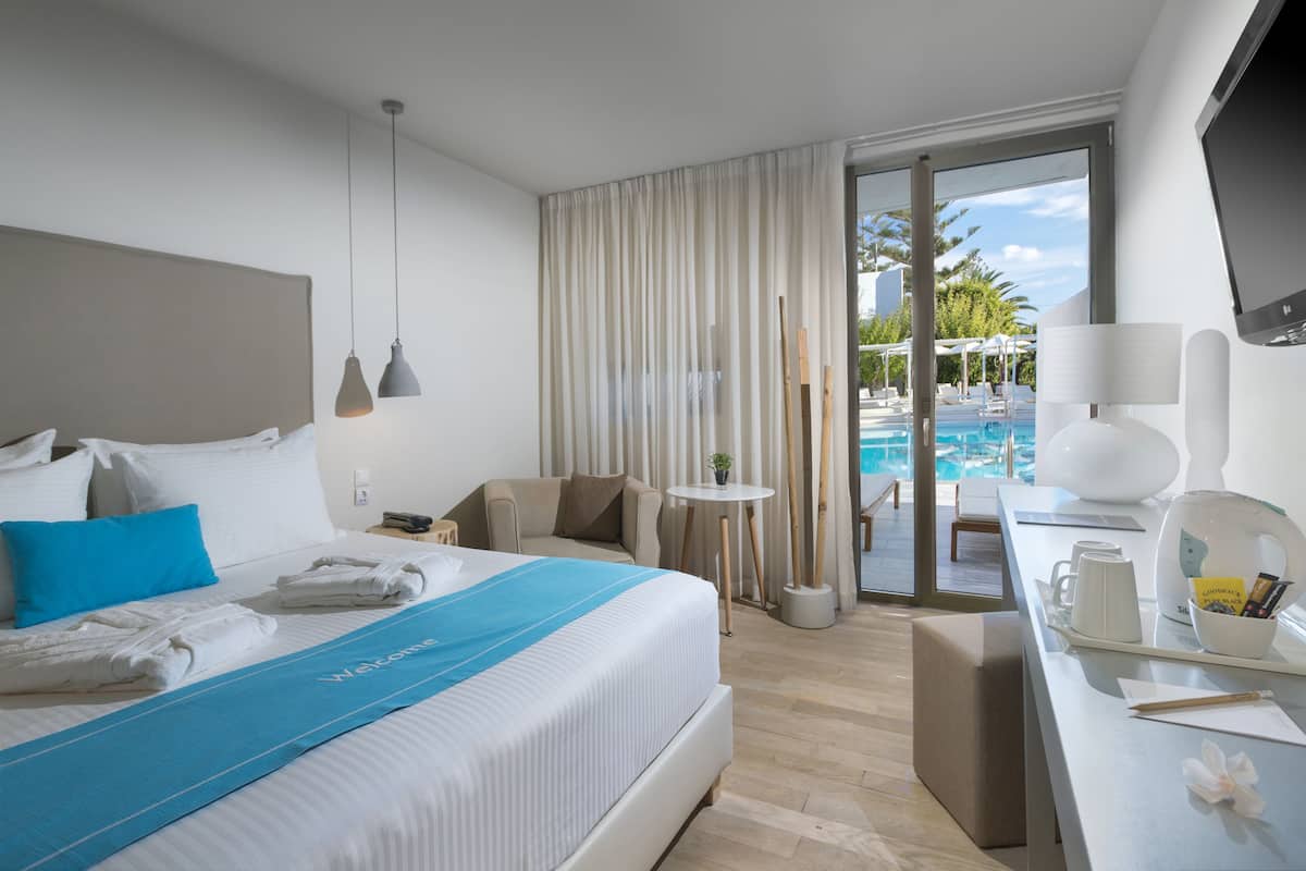 Una habitación de hotel moderna con una cama grande, un escritorio con una computadora portátil, vista a una piscina y un balcón.