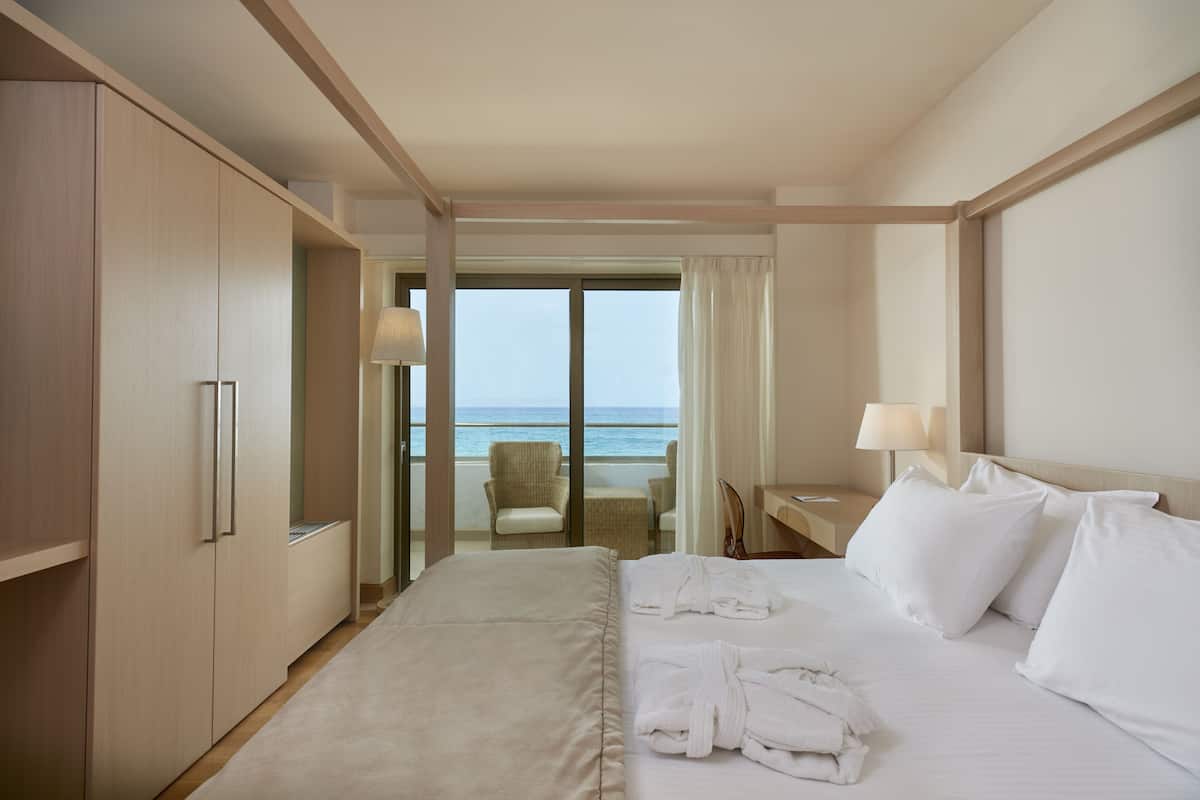 Habitación de hotel con una cama grande, un escritorio, una silla y vista al océano.