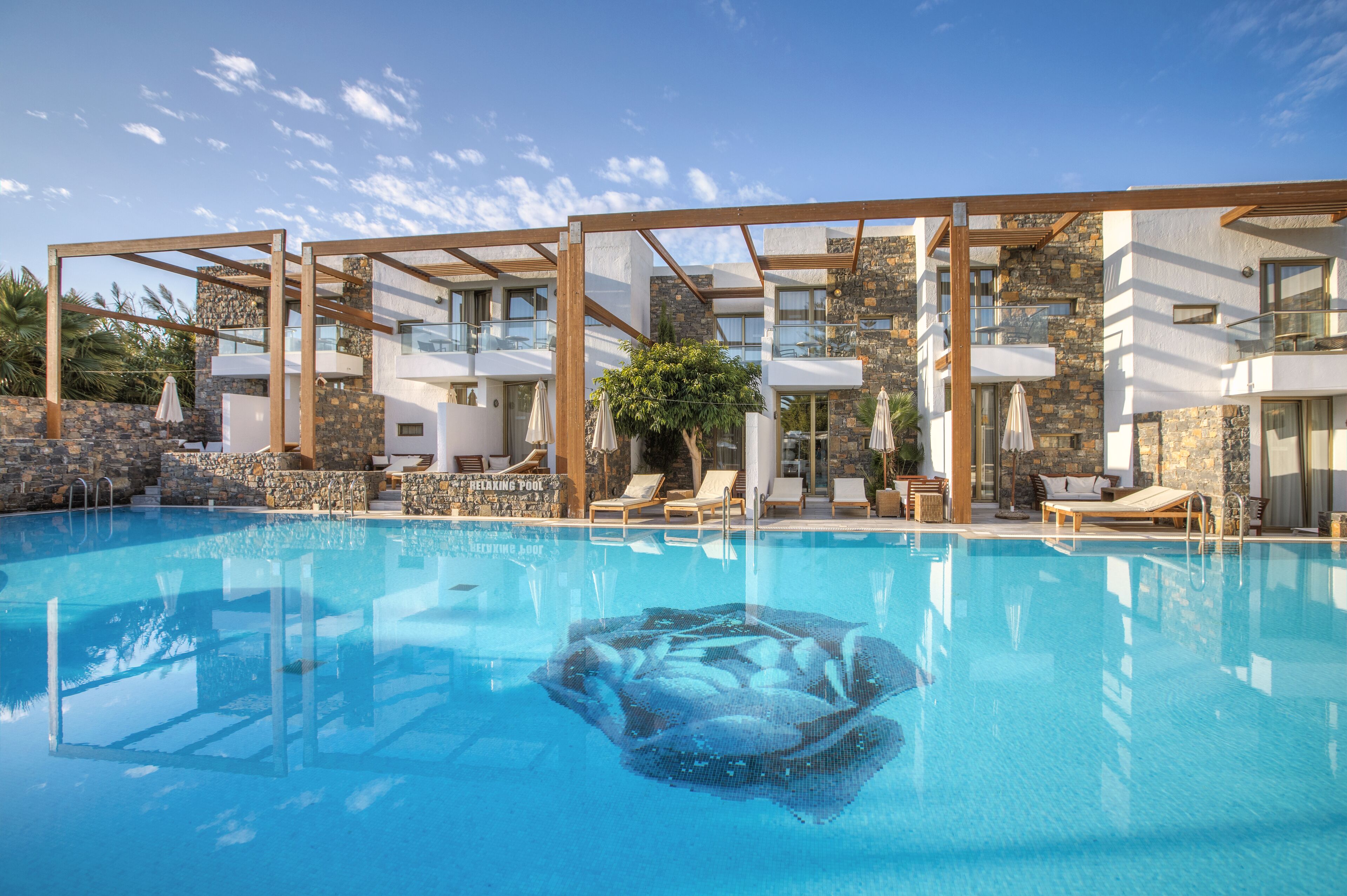 A swimming pool with clear blue water, surrounded by lounge chairs and a wooden pergola structure.
