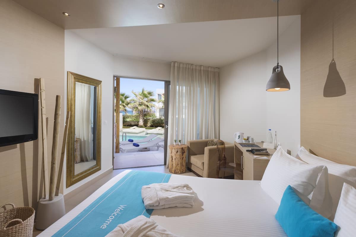 Habitación de hotel con cama, escritorio, silla, televisión y vistas a una piscina y palmeras.