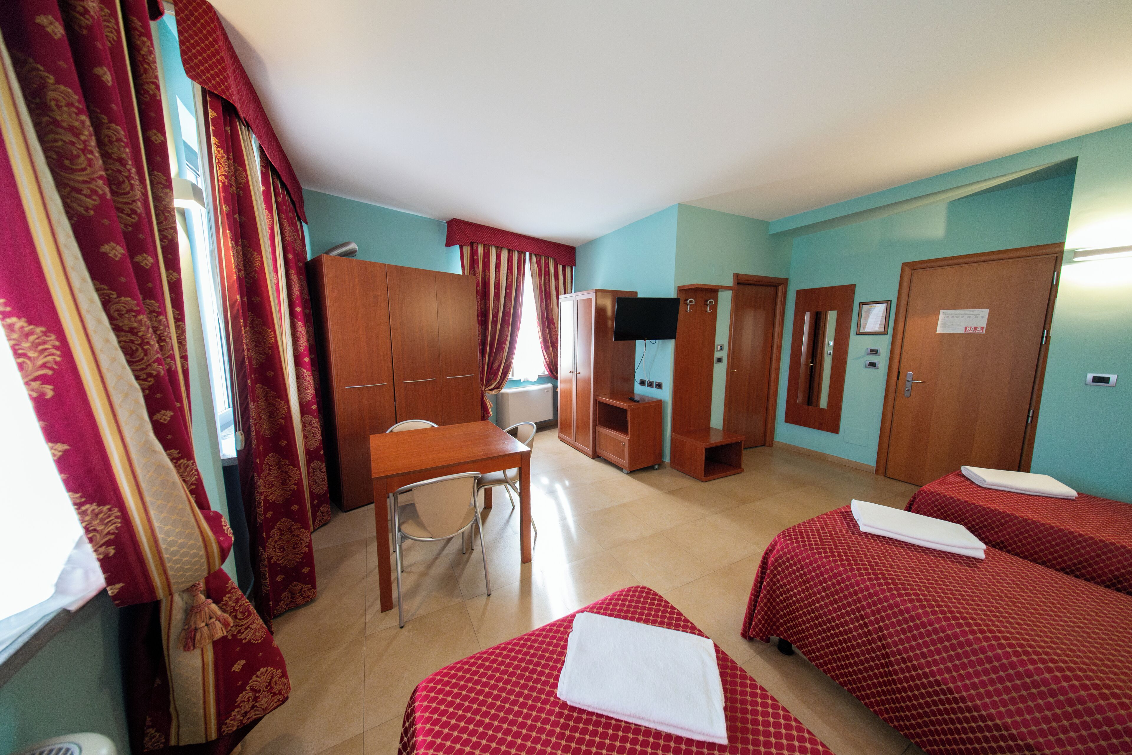 A hotel room with two beds, a desk, a chair, a television, and a wardrobe.