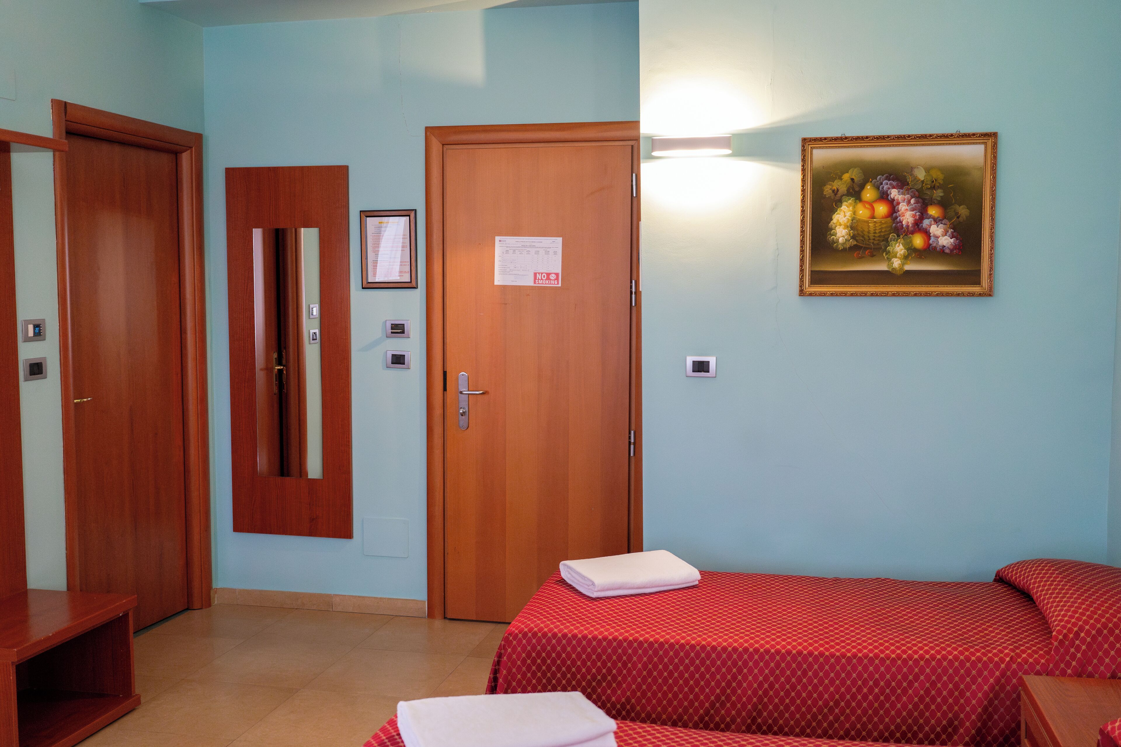 Una camera d'albergo con due letti, una porta in legno, uno specchio e un quadro appeso al muro.