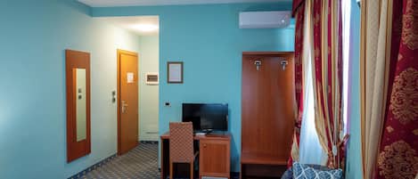 A hotel room with a desk, television, wardrobe, and a patterned carpet.
