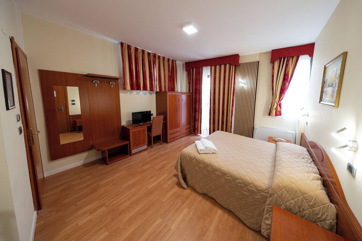 Ein Hotelzimmer mit Bett, Schreibtisch, Kleiderschrank und Fernseher.