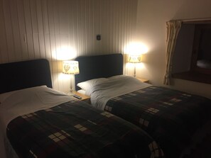 Une chambre d’hôtel avec deux lits, chacun recouvert d’une courtepointe matelassée, une table de chevet avec une lampe et une tête de lit.