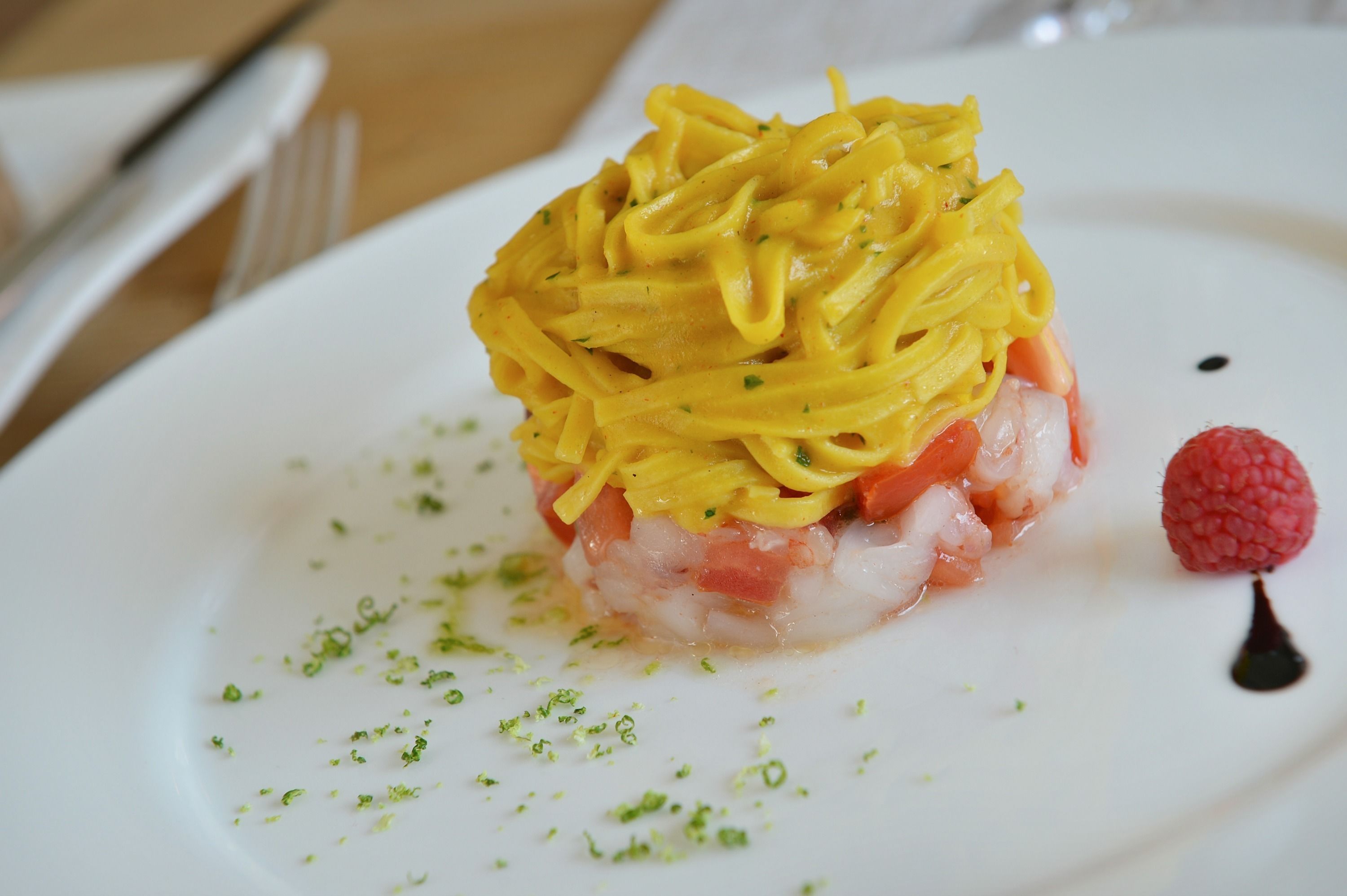 A white plate with a seafood dish, garnished with green herbs and a raspberry.