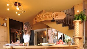 A reception desk with a wooden design, a sign above it, and a potted plant on the right. - Hotel Astra (Livigno)