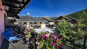 A wooden deck with blue chairs and flower boxes, overlooking a mountain and a building with a sloped roof. - Hotel Astra (Livigno)