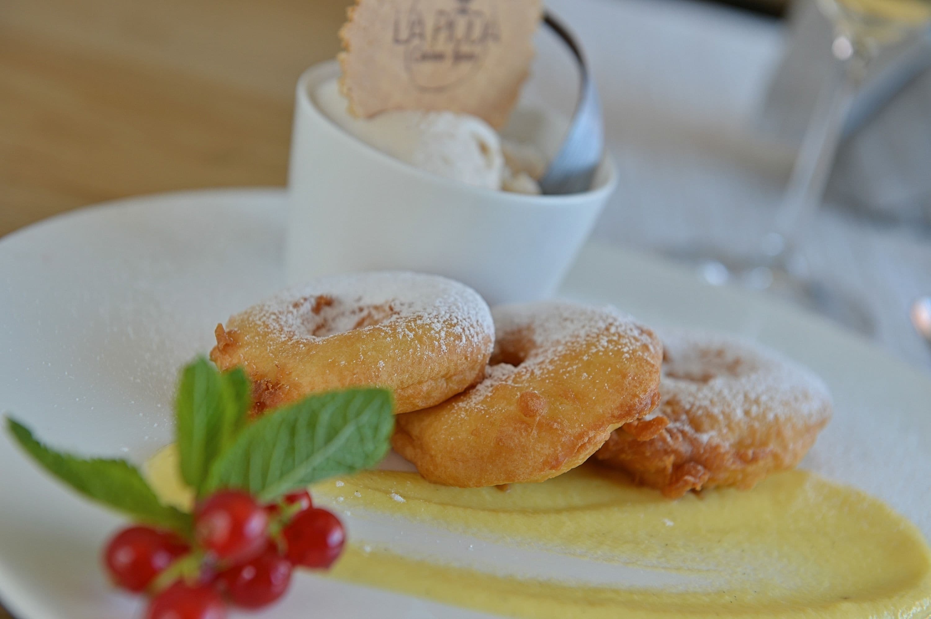 A plate with three donuts, a small cup of ice cream, and a sprig of mint.
