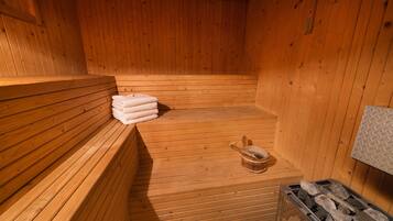 Una sauna de madera con bancos, una pila de toallas y un balde con un cepillo.