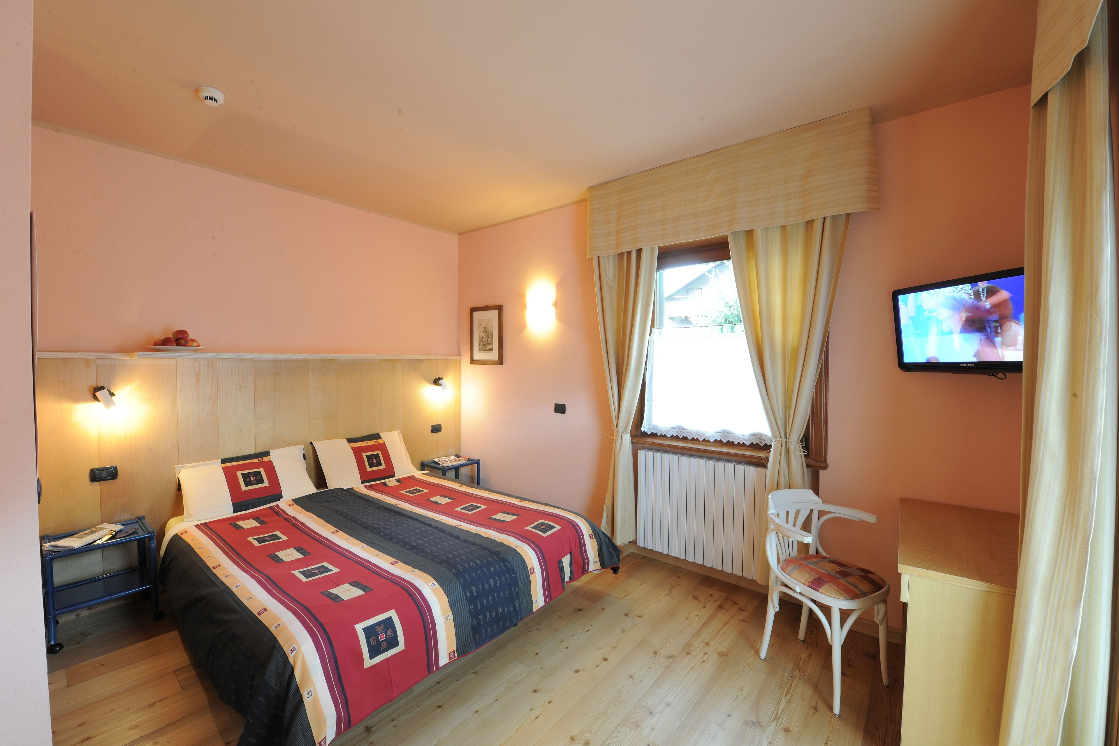 Une chambre à coucher comprenant un lit, des tables de chevet, une chaise, un téléviseur et une fenêtre avec des rideaux.