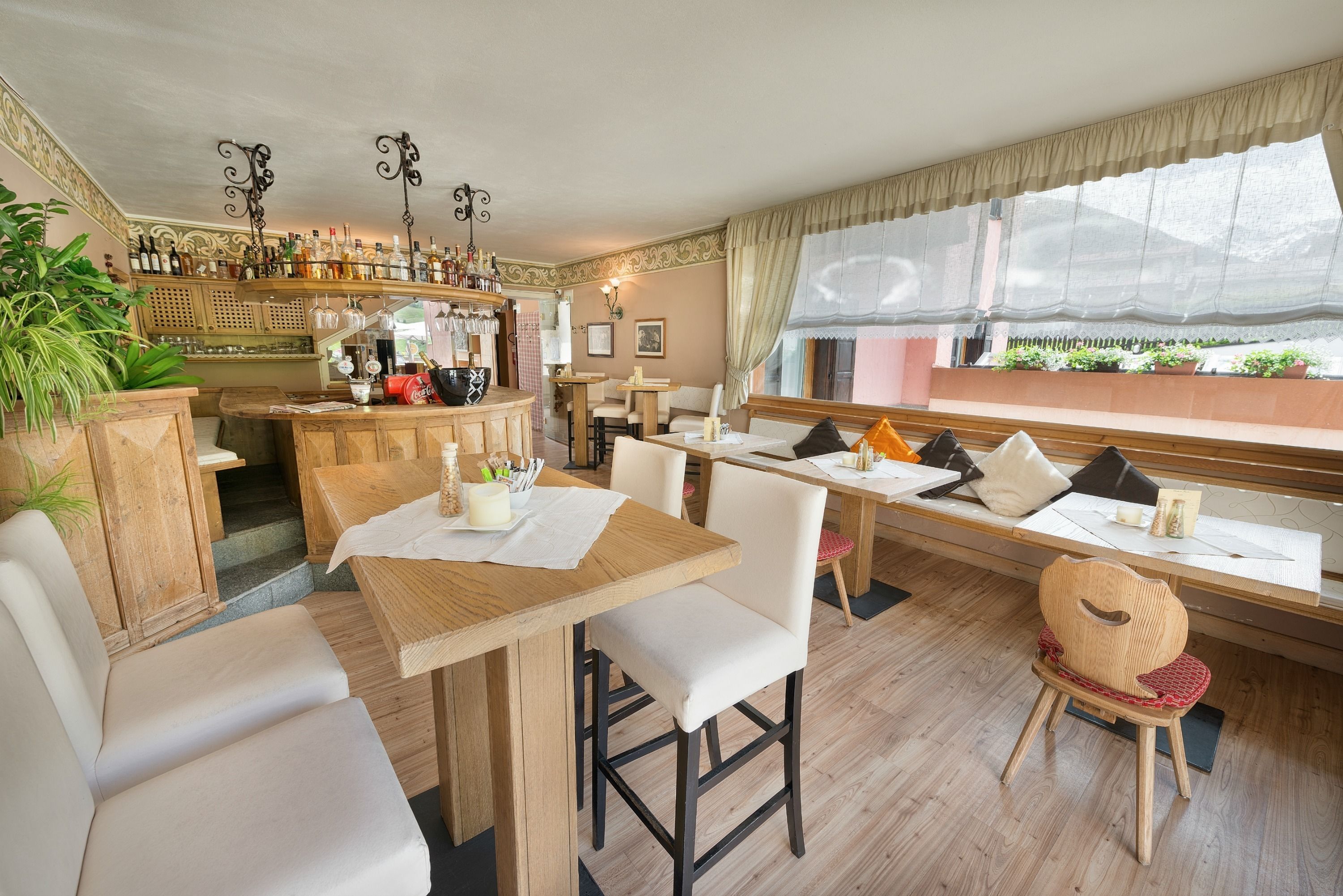 Un ristorante con tavoli e sedie in legno, un'area bar con bottiglie e vista all'esterno attraverso ampie finestre.