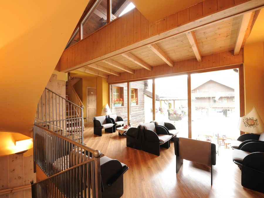 Amplia sala de estar con escalera de madera, varios rincones de descanso y grandes ventanales con vistas al exterior.