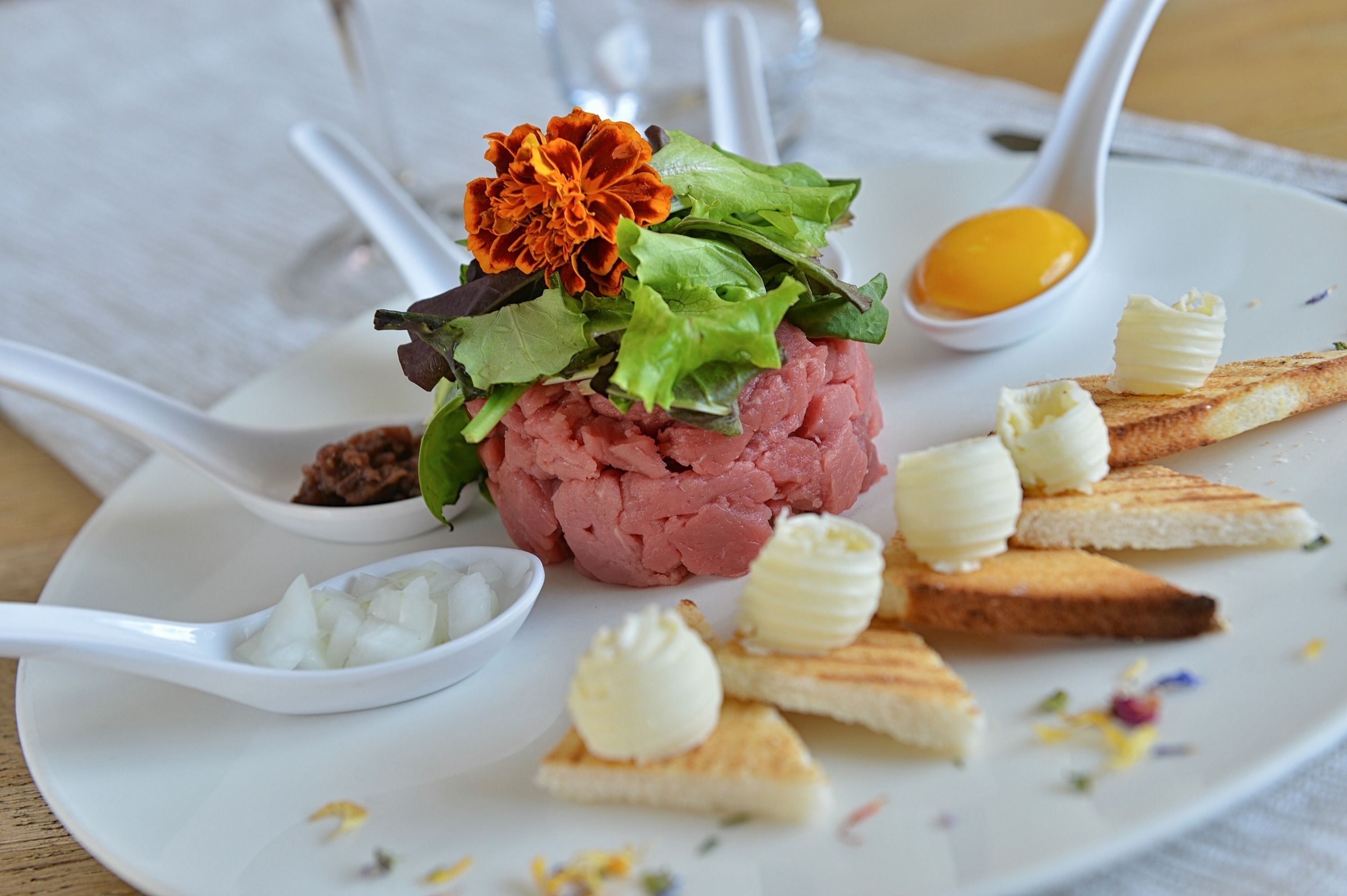 A plate with a meat-based dish, garnished with leafy greens and a flower, accompanied by butter cubes and bread slices.