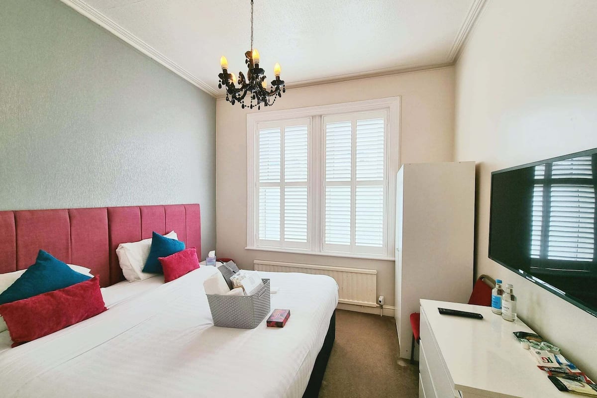 A hotel room with a large bed, a TV, and a window with blinds.
