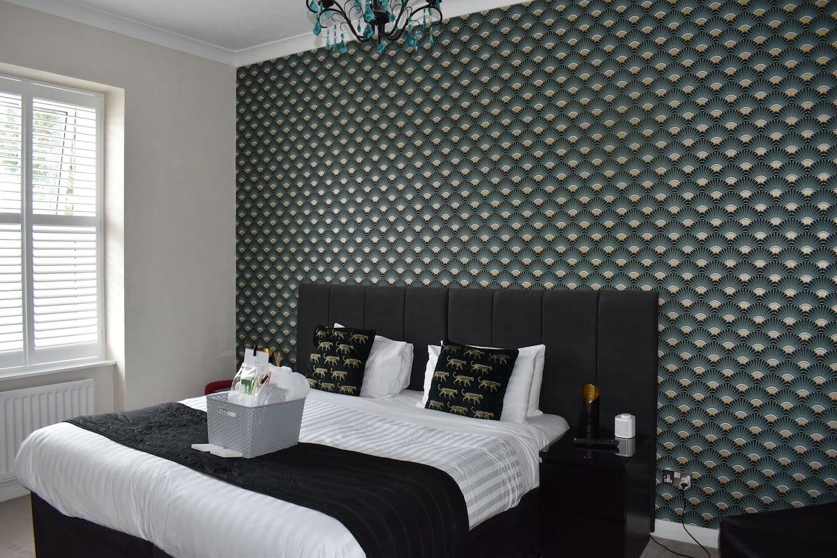 A neatly made bed with a black headboard, white bedding, and decorative pillows. A bedside table with a lamp and a small plant is visible.
