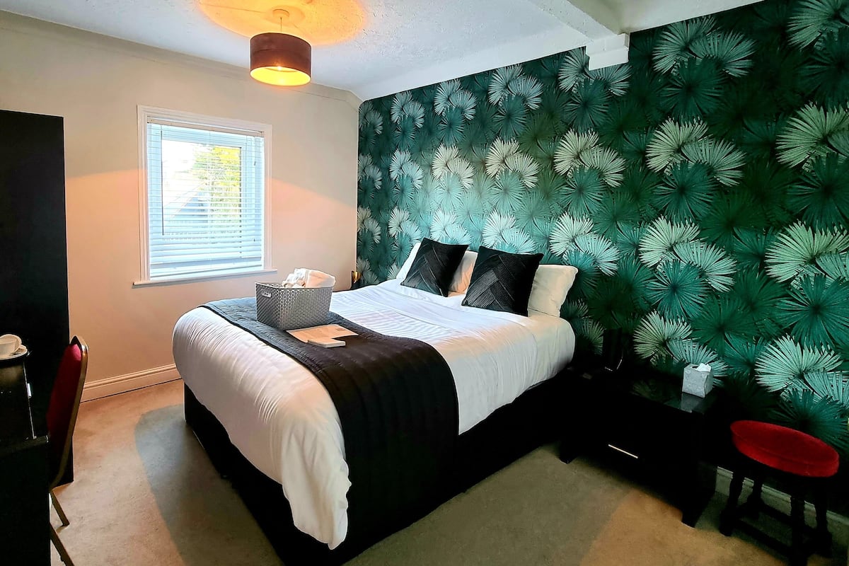 A neatly made bed with a white and black bedspread, a bedside table with a lamp, and a chair.