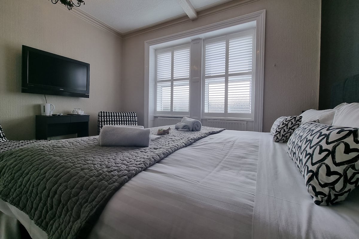 A neatly arranged bedroom with a bed, a bedside table, a television, and a window with blinds.