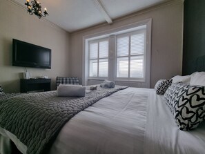 Un dormitorio ordenado con cama, mesita de noche, televisor y ventana con persianas.