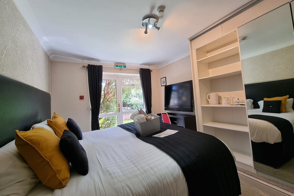 A hotel room with a bed, a television, a wardrobe, and a view of the outdoors.