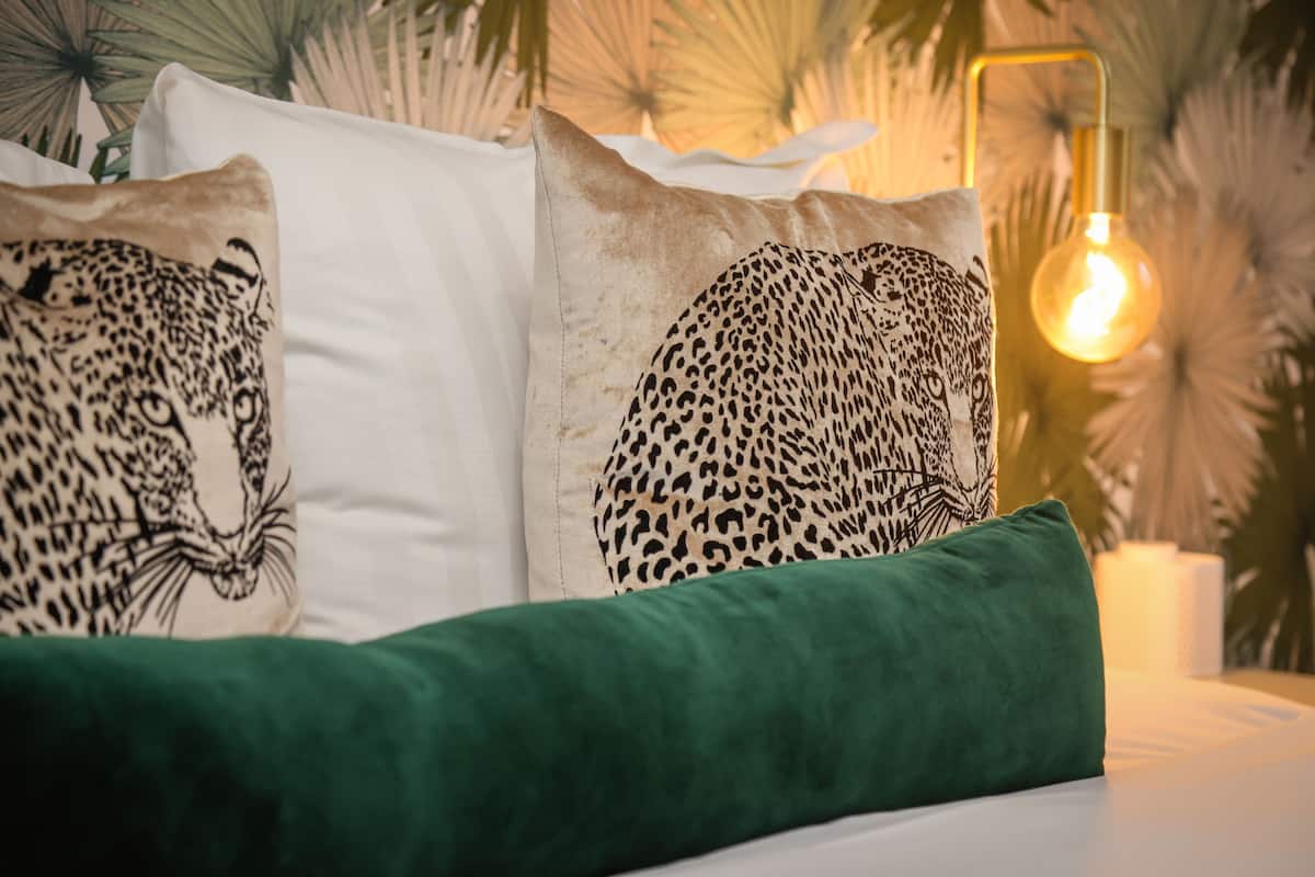 A bed with leopard print pillows, a green pillow, and a warm light fixture.