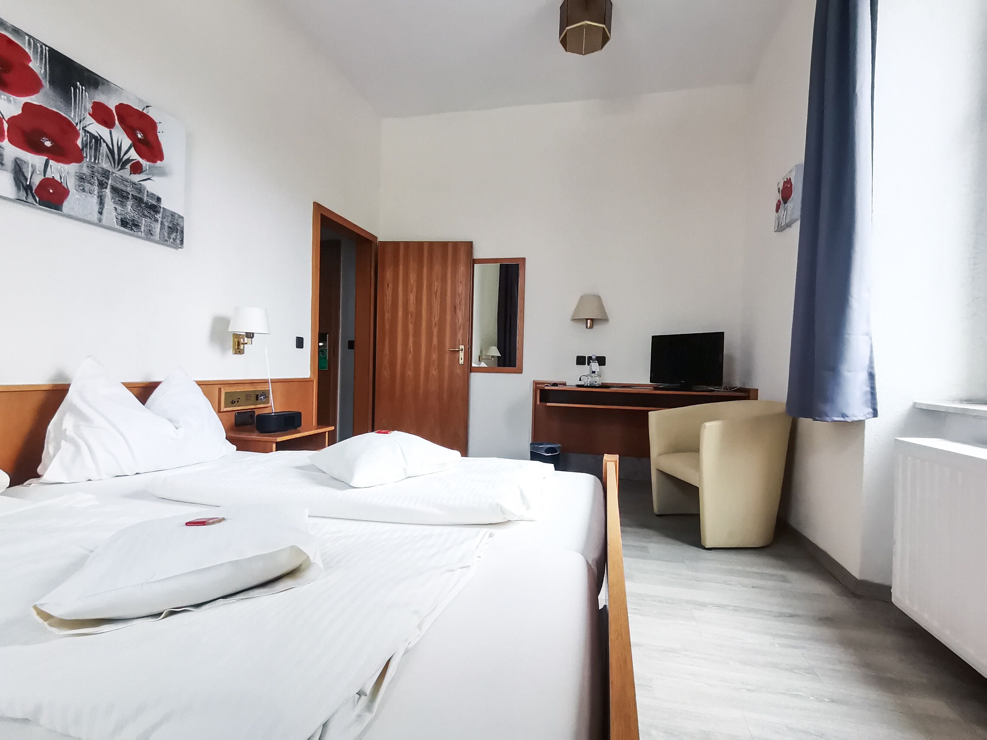 Camera d'albergo con un letto, una scrivania, una sedia, una televisione e un quadro appeso al muro.
