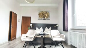 Habitación de hotel con cama, dos sillones, una mesa, una lámpara en el techo, un radiador y una ventana con cortinas.