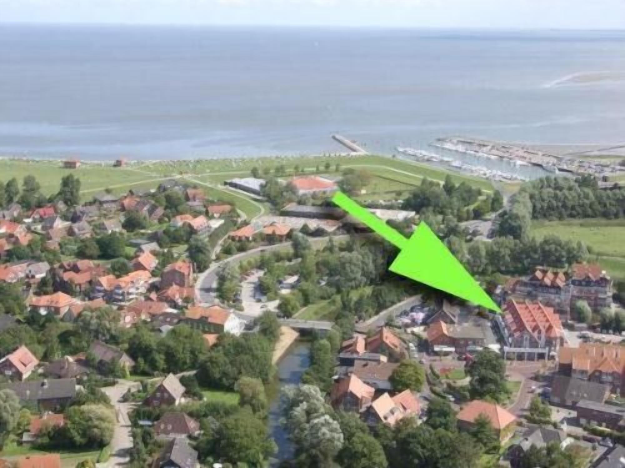 An aerial view of a residential area with houses, a river, and a green arrow pointing to a specific location.