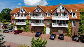 A row of brick houses with attached balconies, a paved driveway, and parked cars.
