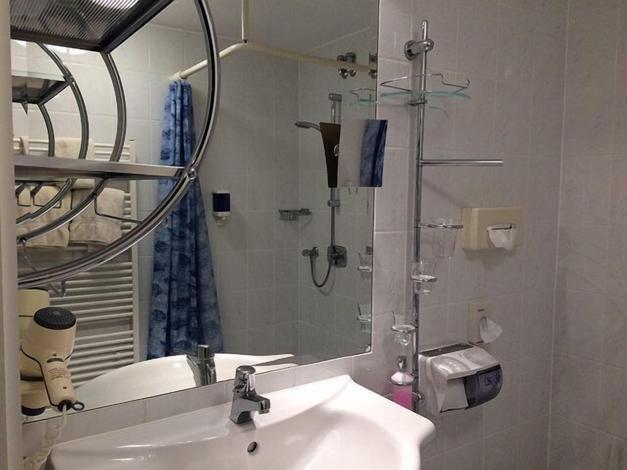 A bathroom with a sink, mirror, shower, and towel rack.