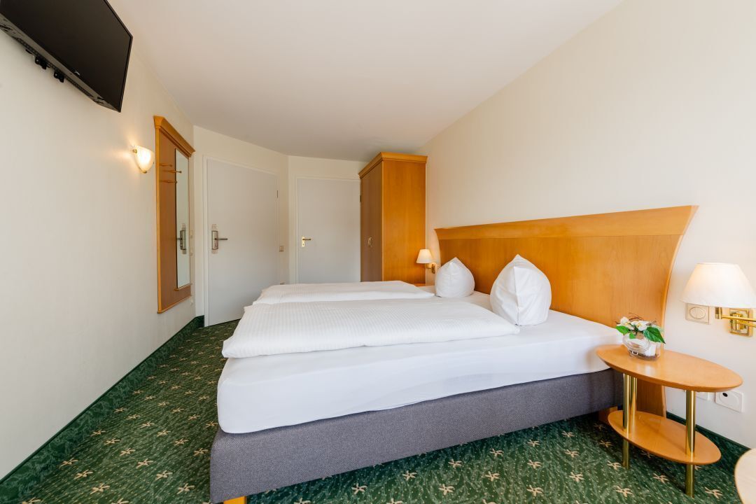 A hotel room with a large bed, a wooden headboard, a small table with a lamp, and a mirror on the wall.
