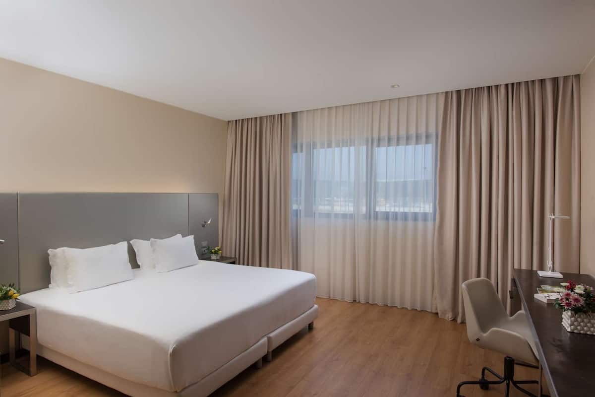 Ein Hotelzimmer mit einem großen Bett, einem Schreibtisch mit Stuhl und einem Fenster mit Vorhängen.