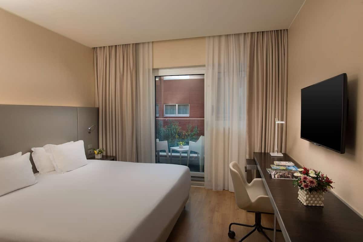 Ein Hotelzimmer mit einem Bett, einem Schreibtisch mit Stuhl, einem Flachbildfernseher und einem Fenster mit Vorhängen.