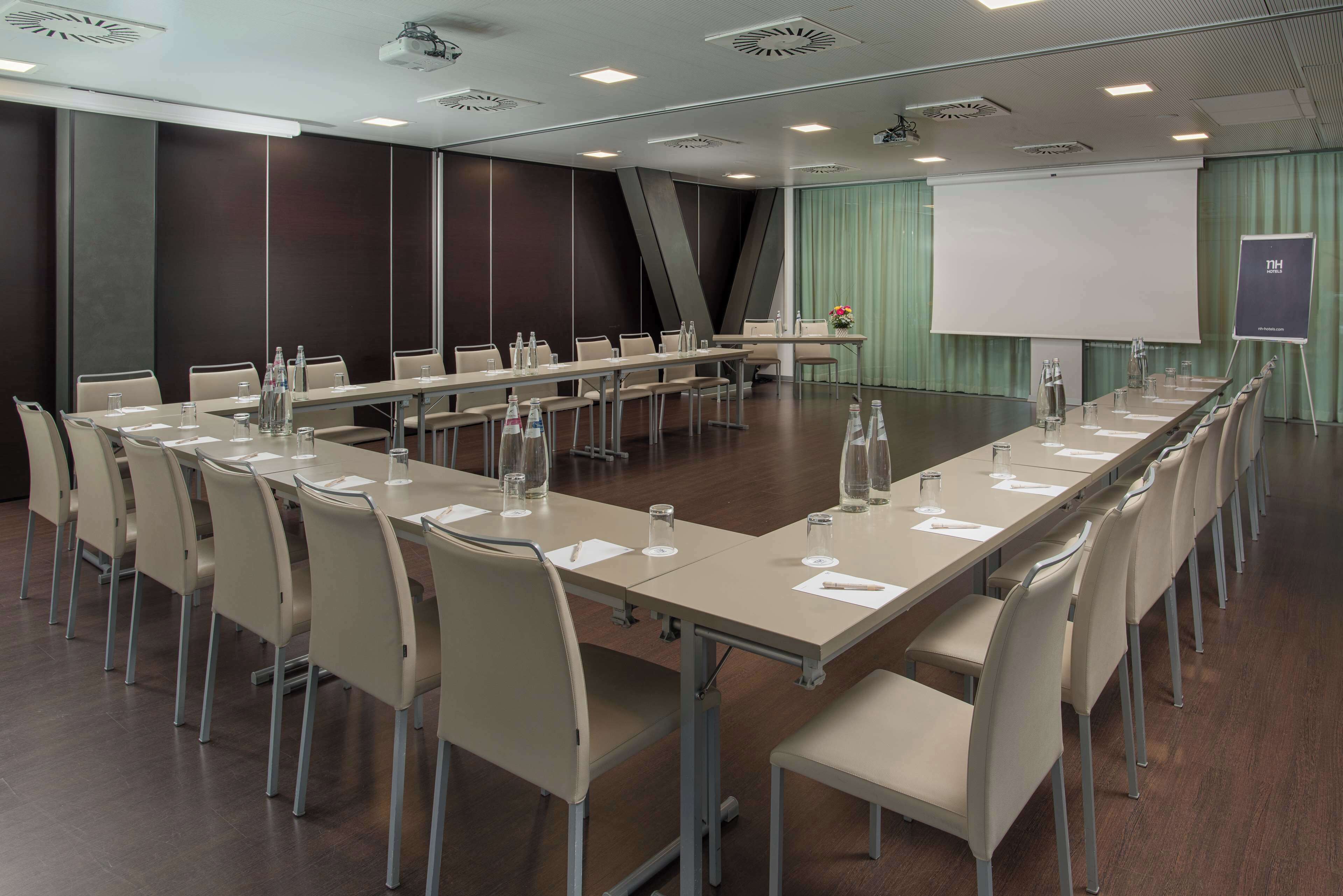 A conference room with a long table, chairs, a projector screen, and a presentation stand.