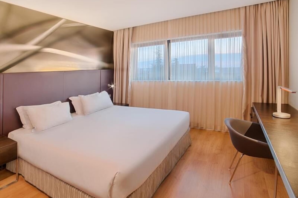 A hotel room with a large bed, a desk, and a view of the outdoors.