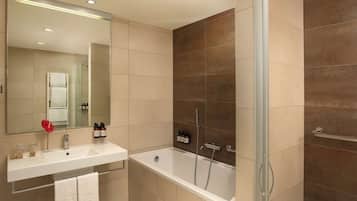 Un baño moderno con lavamanos, espejo y bañera blancos. Hay artículos de aseo en el lavamanos y un perchero en la pared.