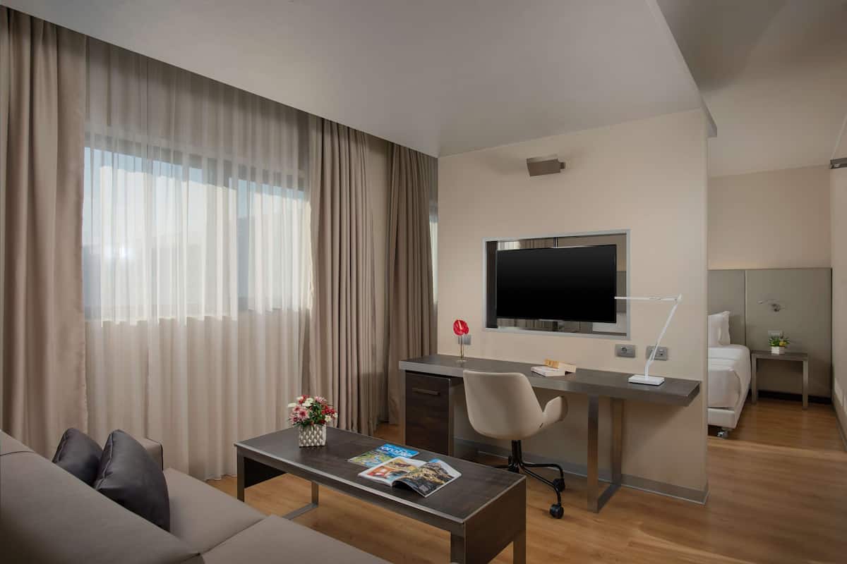 Ein modernes Hotelzimmer mit einer Couch, einem Schreibtisch mit Computer, einem Fernseher und einem Bett.