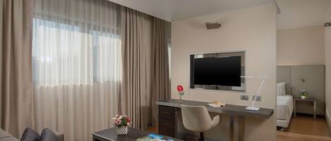 Habitación de hotel moderna con sofá, escritorio con computadora, televisor y cama.