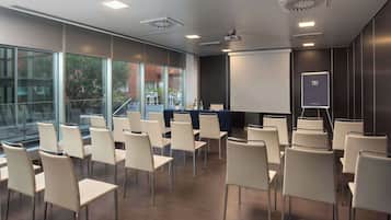 Un salón de conferencias con filas de sillas, una pantalla de proyector y una pizarra para presentaciones.