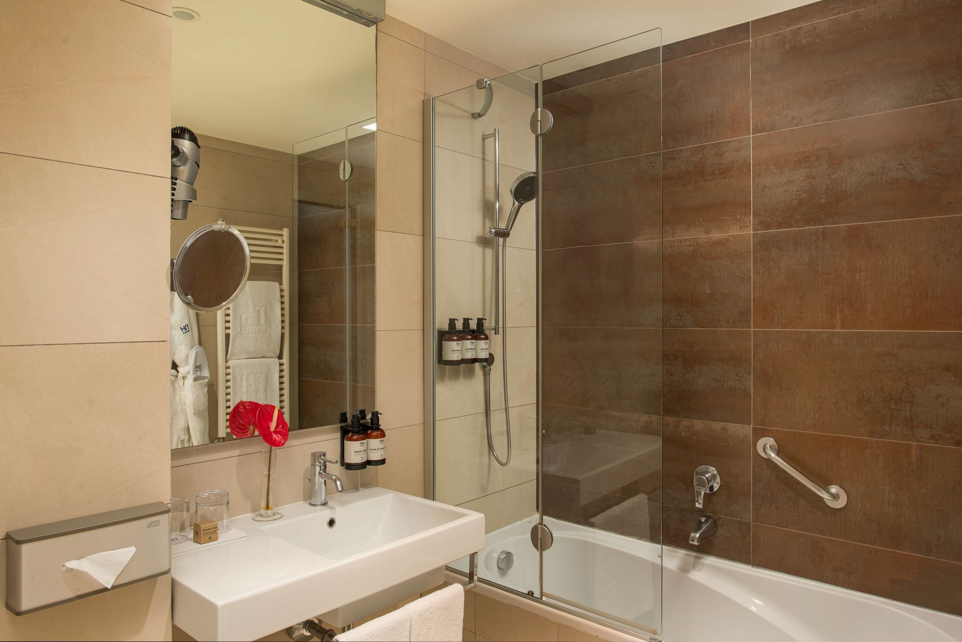 A modern bathroom with a glass-enclosed shower, a white sink, and a large mirror.