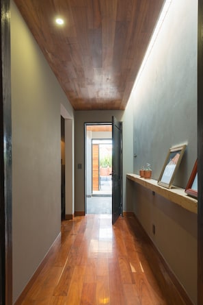 A hallway with wooden flooring, a ceiling with a recessed light, and a door leading to an outdoor area.