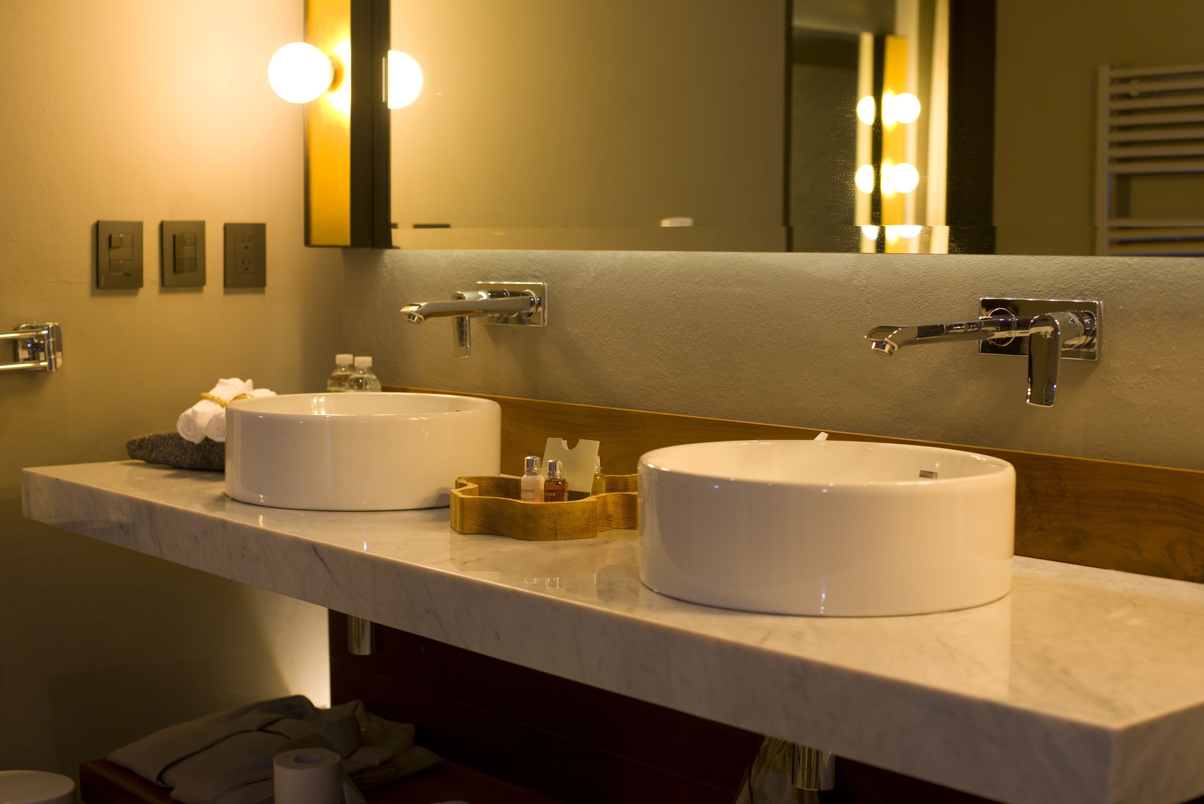 A bathroom with two white sinks, a mirror, and a vanity with toiletries.