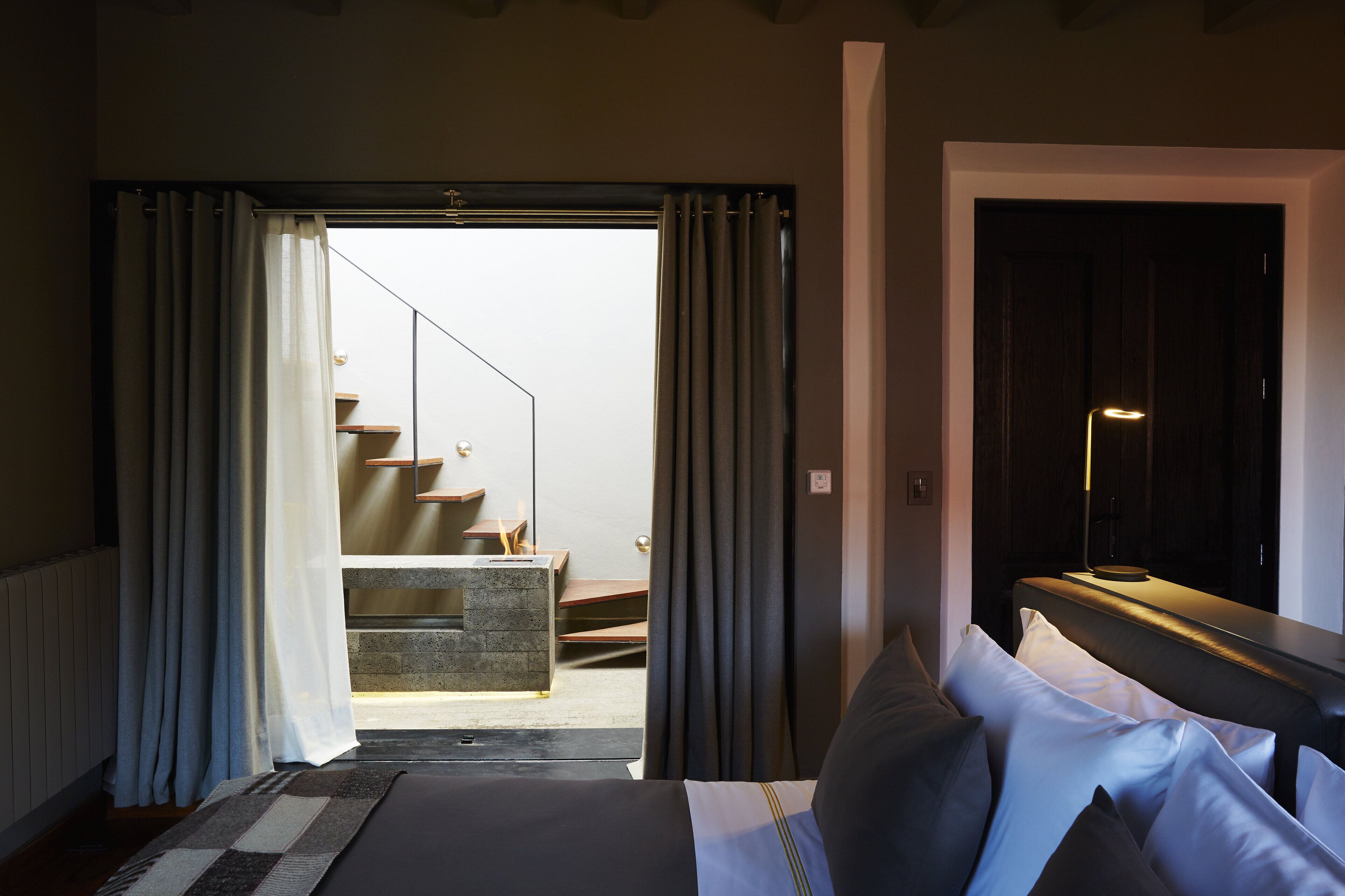 A hotel room with a bed, a nightstand, and a view of a staircase leading to a balcony.