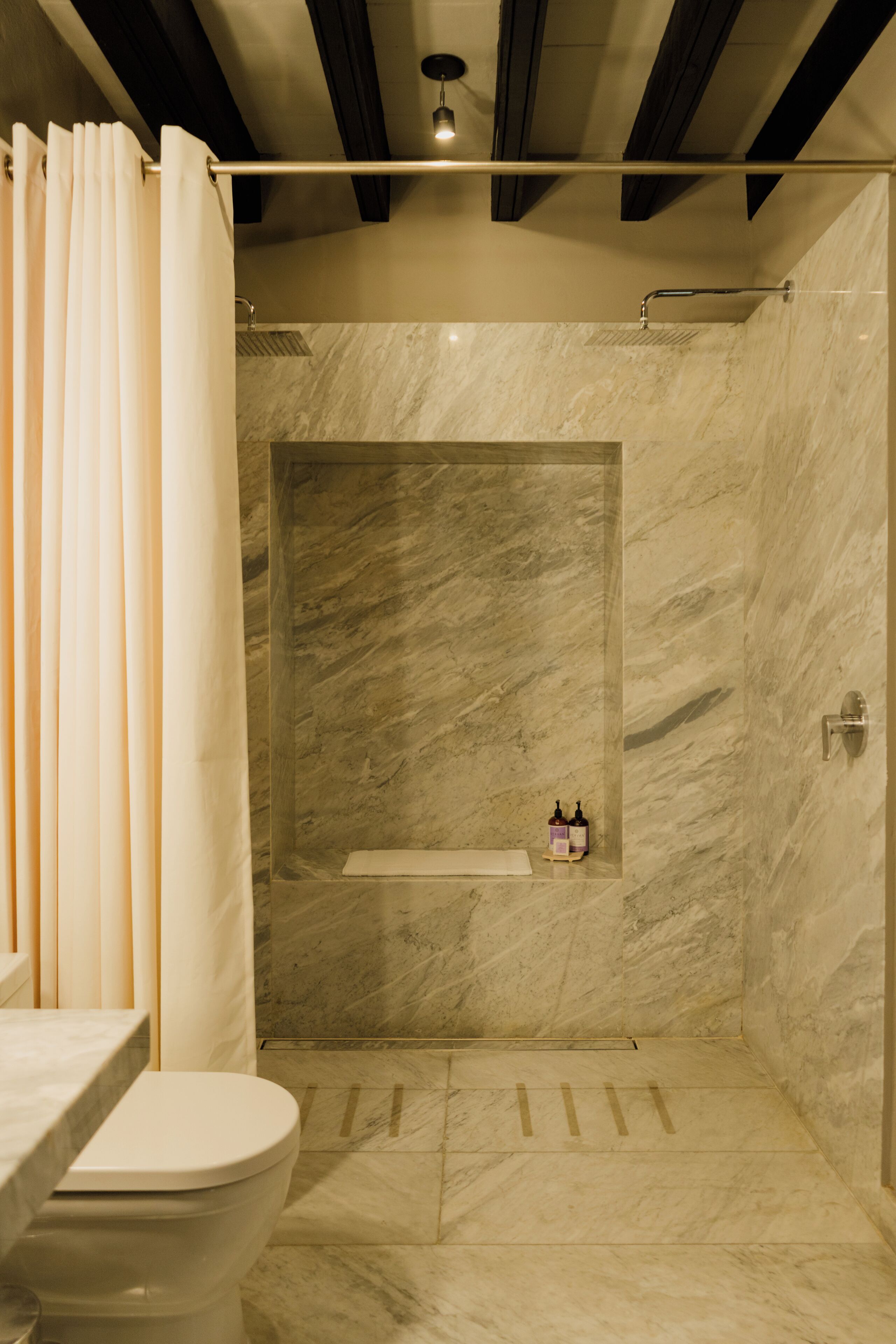 A bathroom with a shower, toilet, and a shelf with toiletries.
