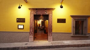A yellow building with an entrance featuring a stone archway. There are signs on the wall indicating 'Aperi Restaurant' and 'De Casa'. - Dos Casas Hotel & Spa (San Miguel de Allende)